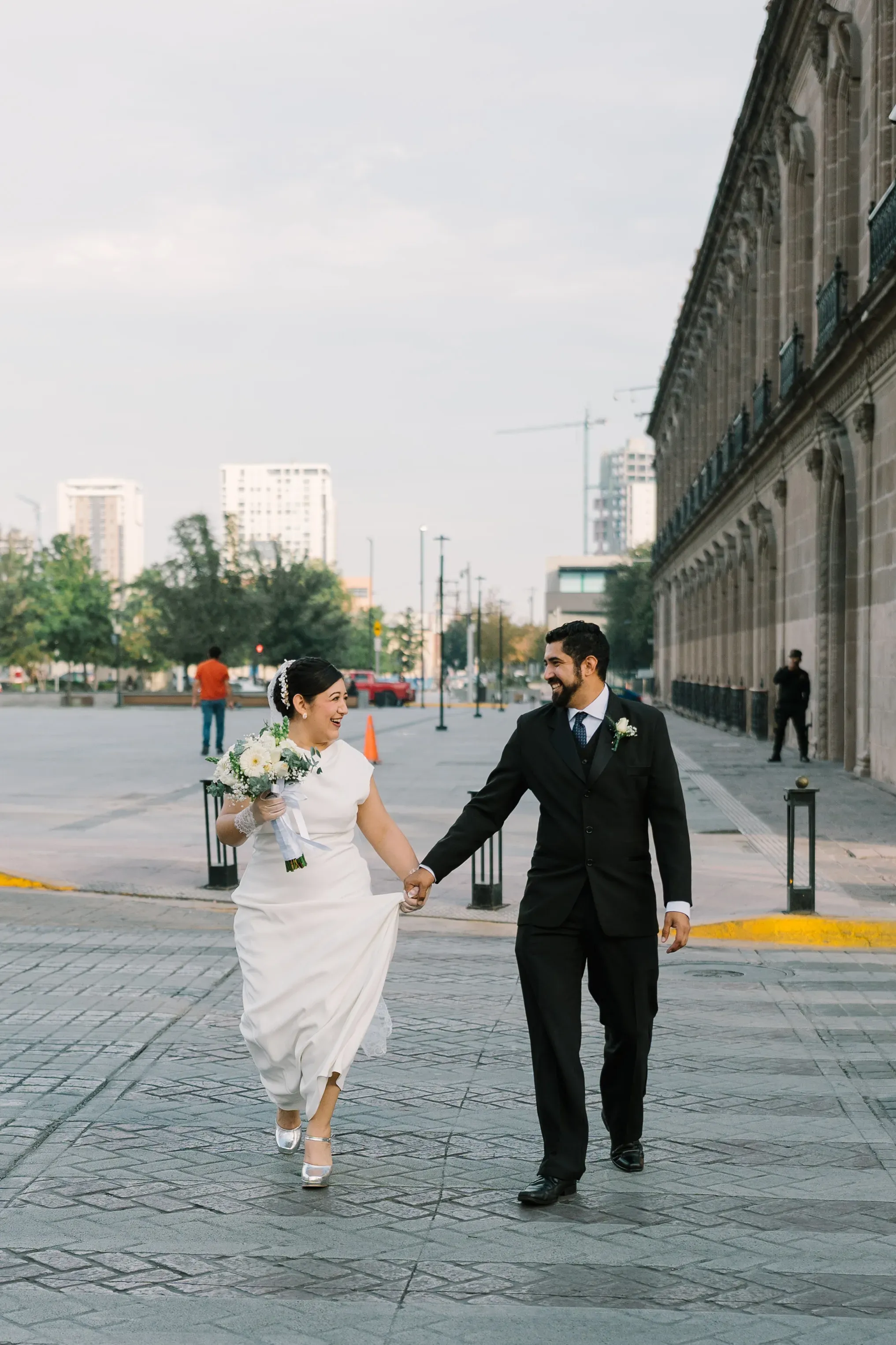 Amy y Jorge tomados de la mano caminando felices por calle empedrada frente a edificio histórico del centro de Monterrey