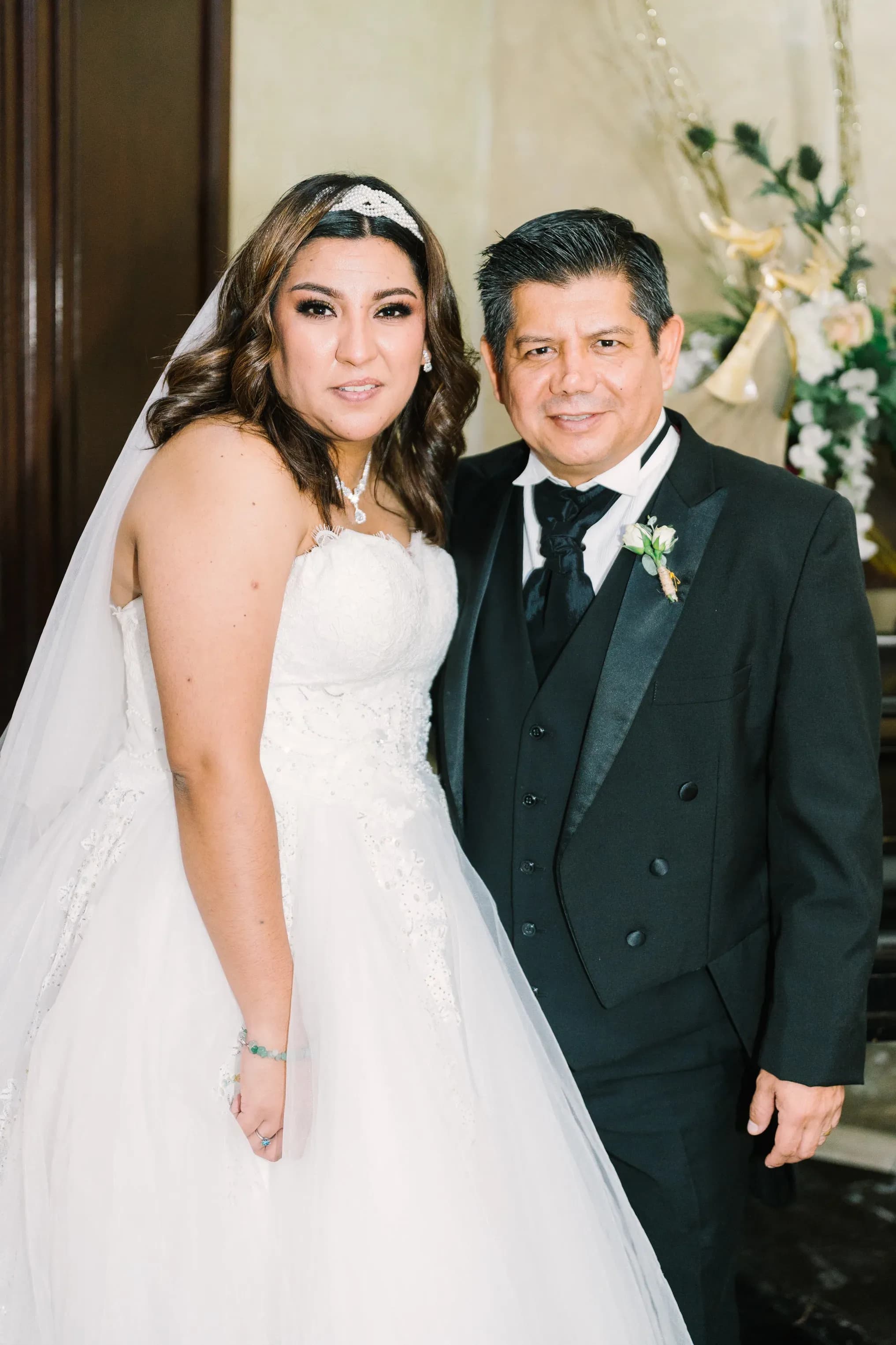 Novia con vestido de princesa y velo junto a hombre de traje negro en ceremonia de boda