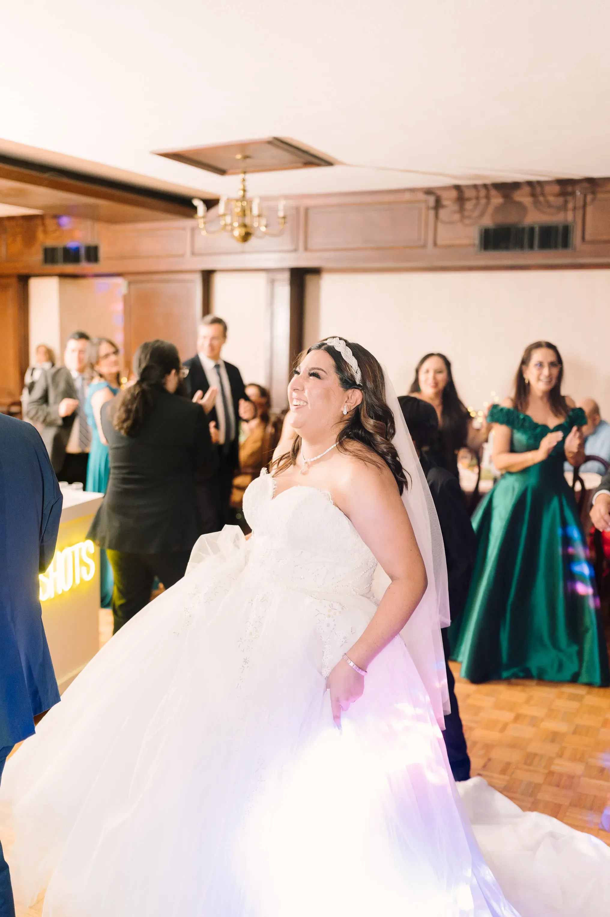 Novia sonriendo y girando en pista de baile durante recepción de boda con letrero SHOTS