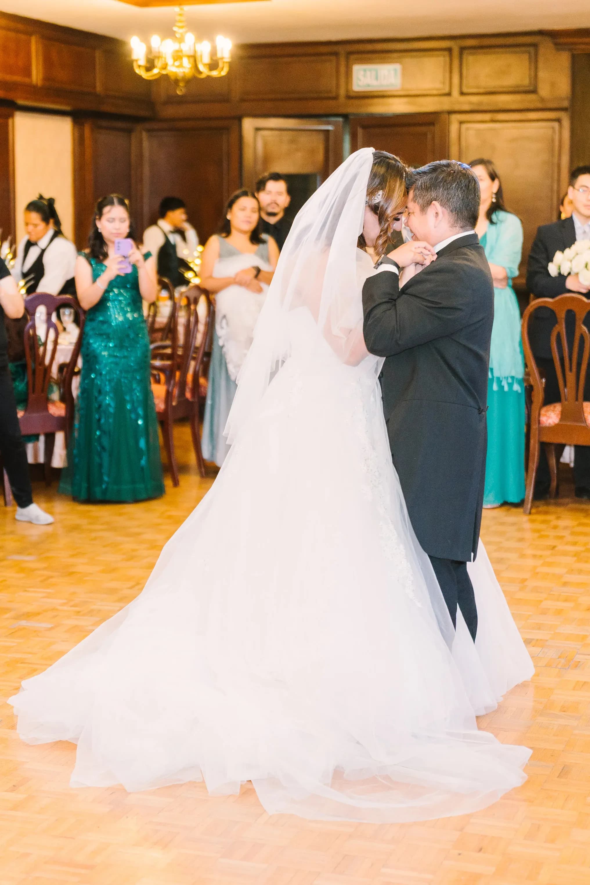 Pareja de novios bailando vals en salón de boda con invitados observando al fondo