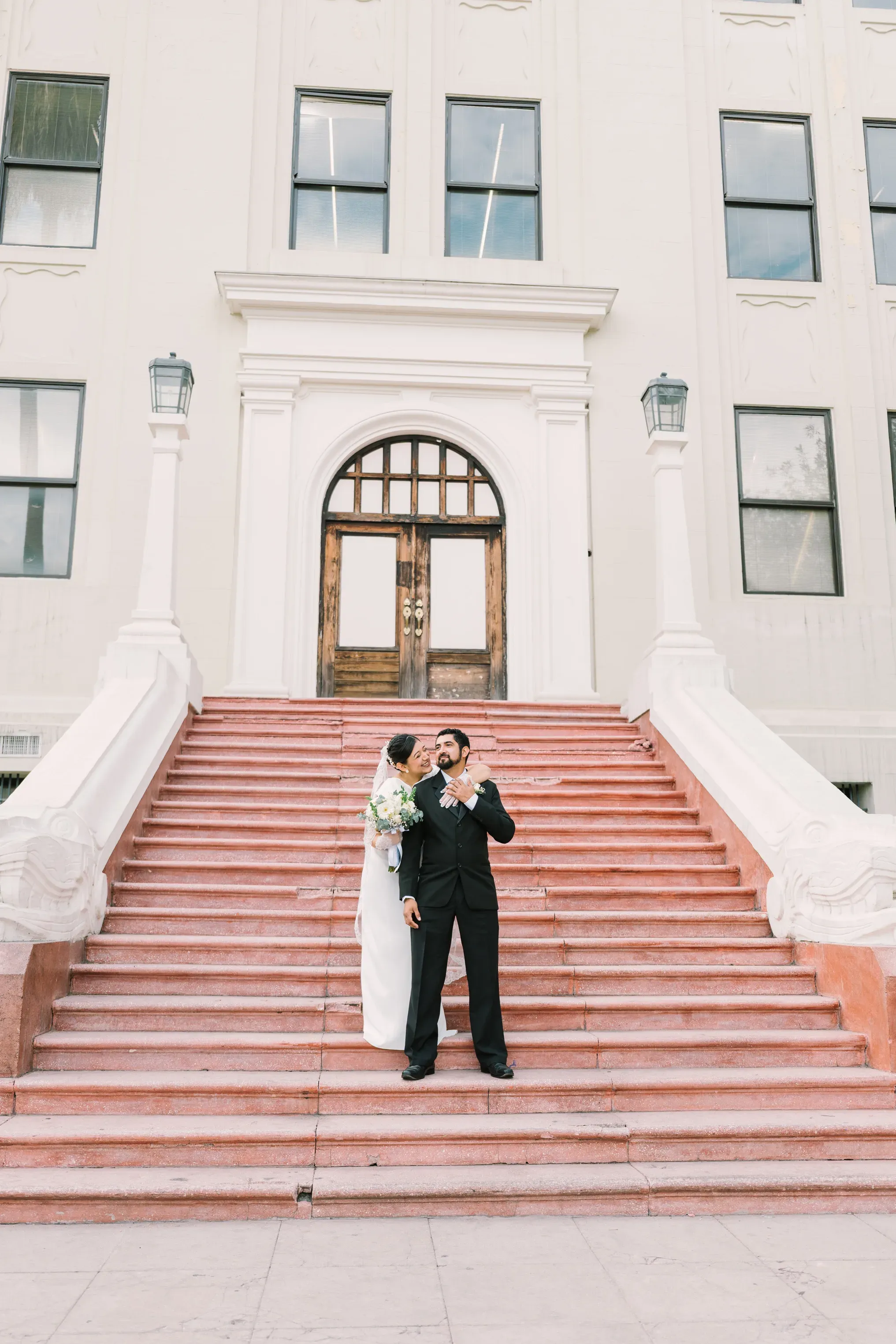Pareja de novios posando abrazados en escalinata monumental de edificio neoclásico