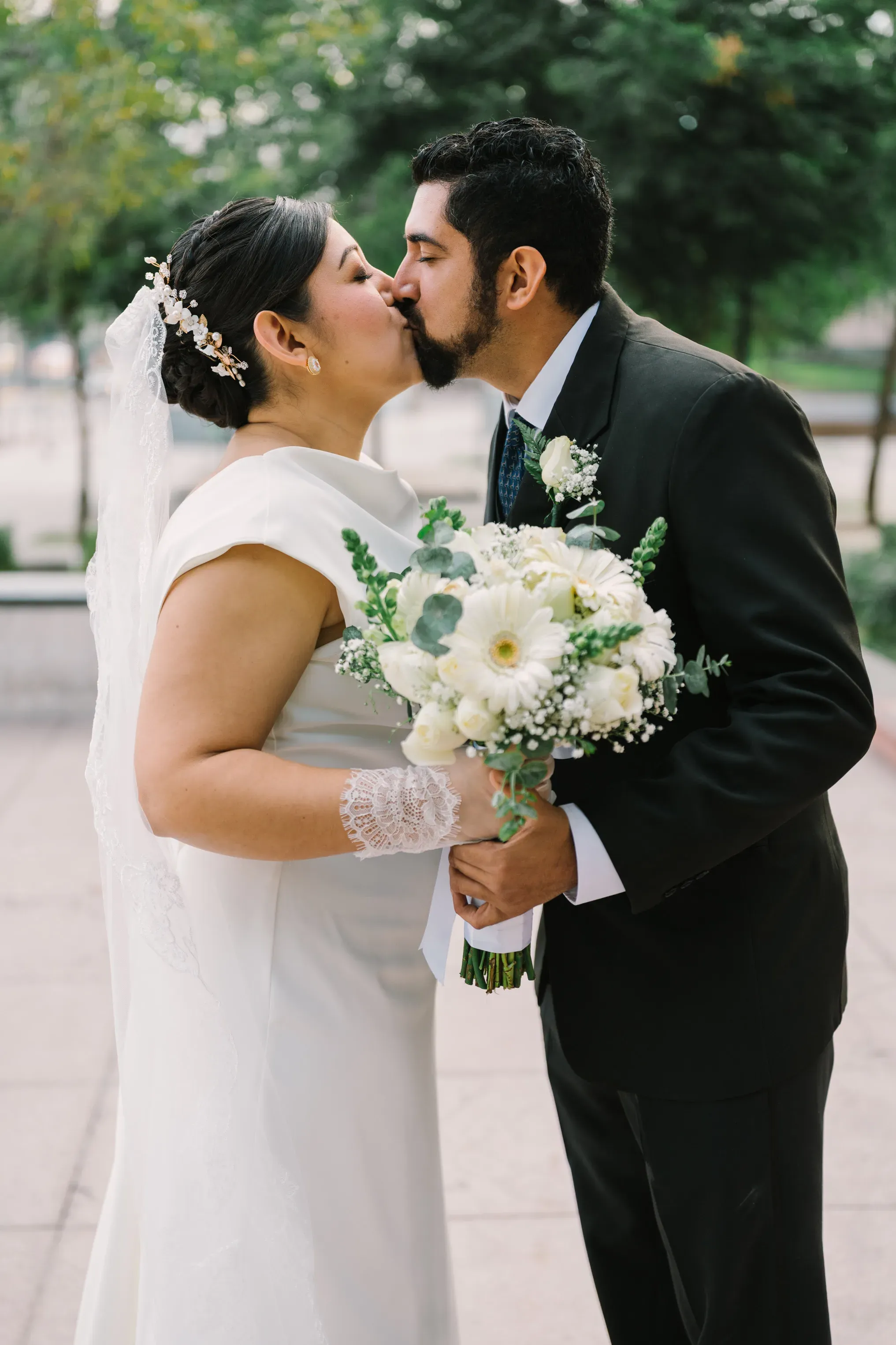 Novios besándose con ramo de flores blancas y eucalipto en sesión fotográfica al aire libre