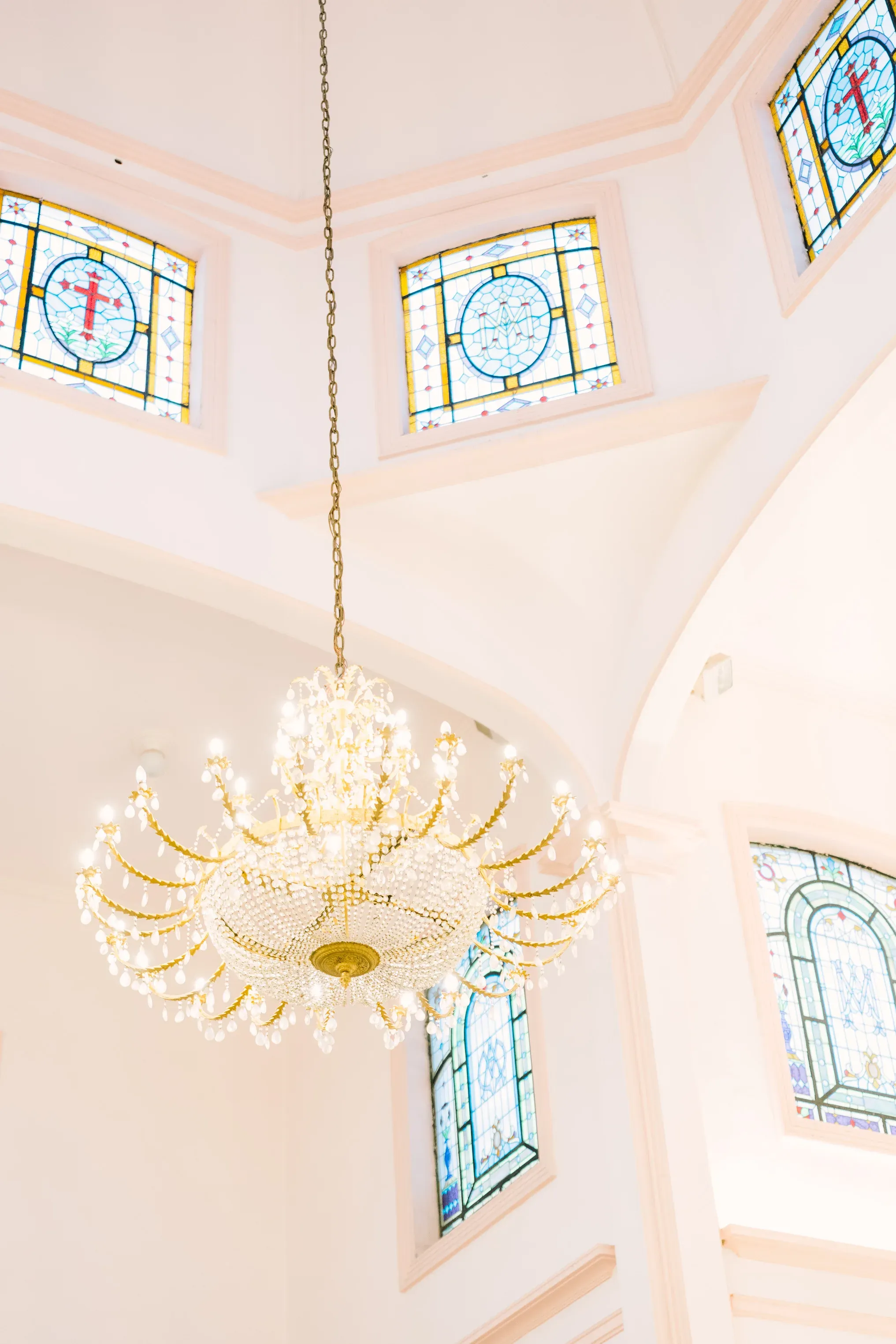 Candelabro de cristal dorado colgante en iglesia con vitrales coloridos de cruces y motivos religiosos