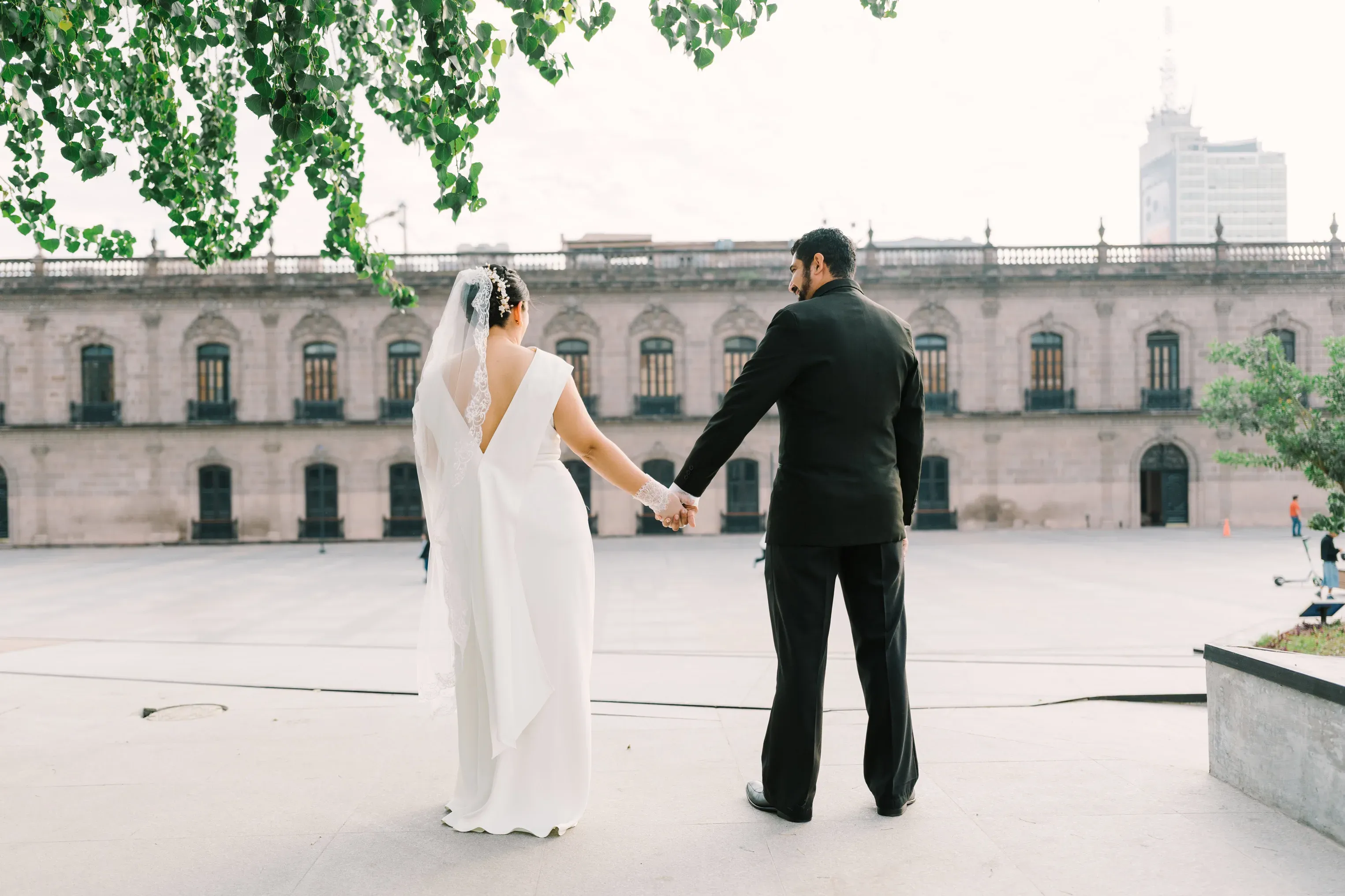 Pareja de novios de espaldas tomados de la mano frente al Palacio de Gobierno de Monterrey
