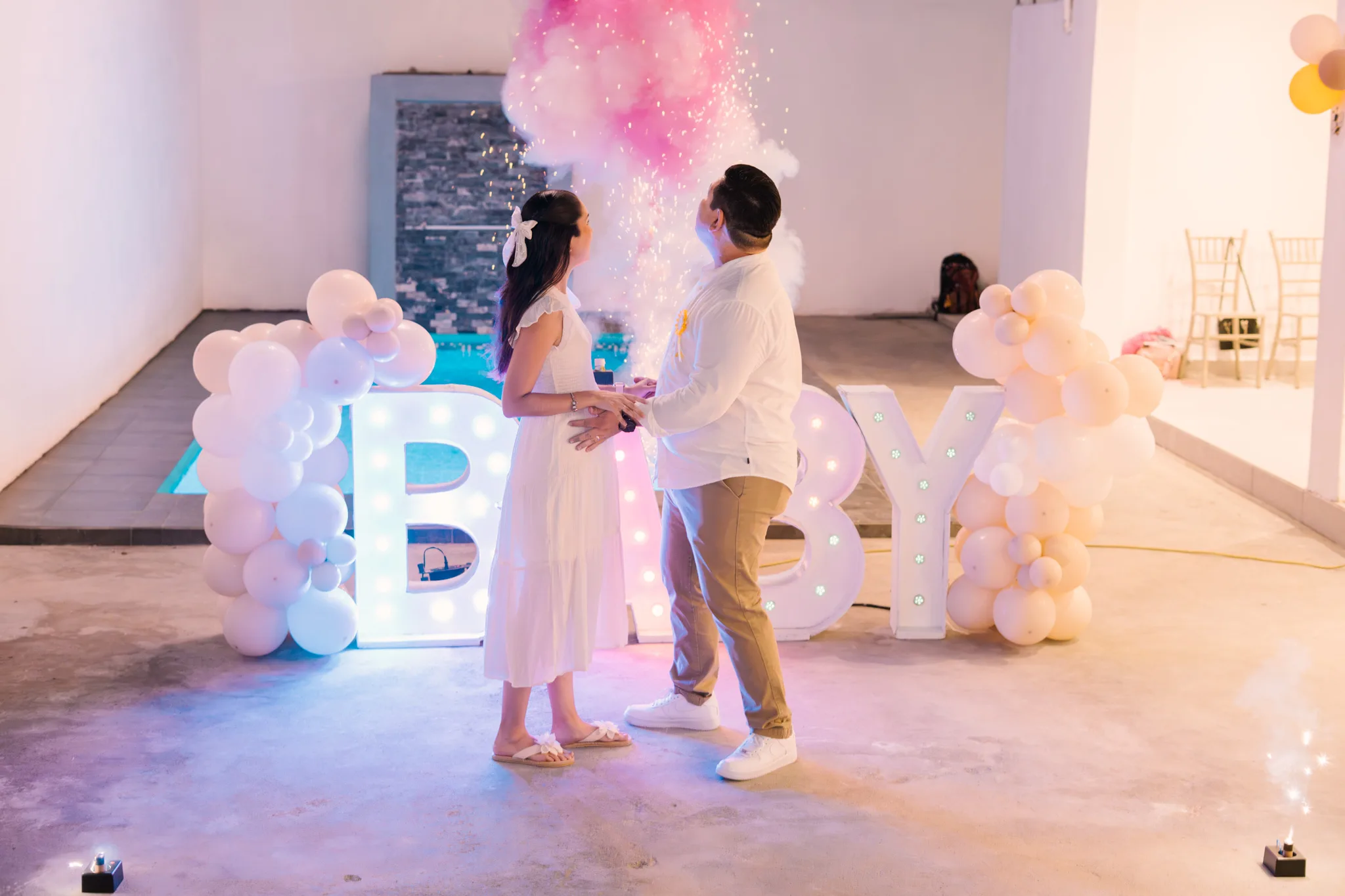 Pareja descubriendo el sexo de su bebé con humo rosa en fiesta gender reveal con letrero BABY