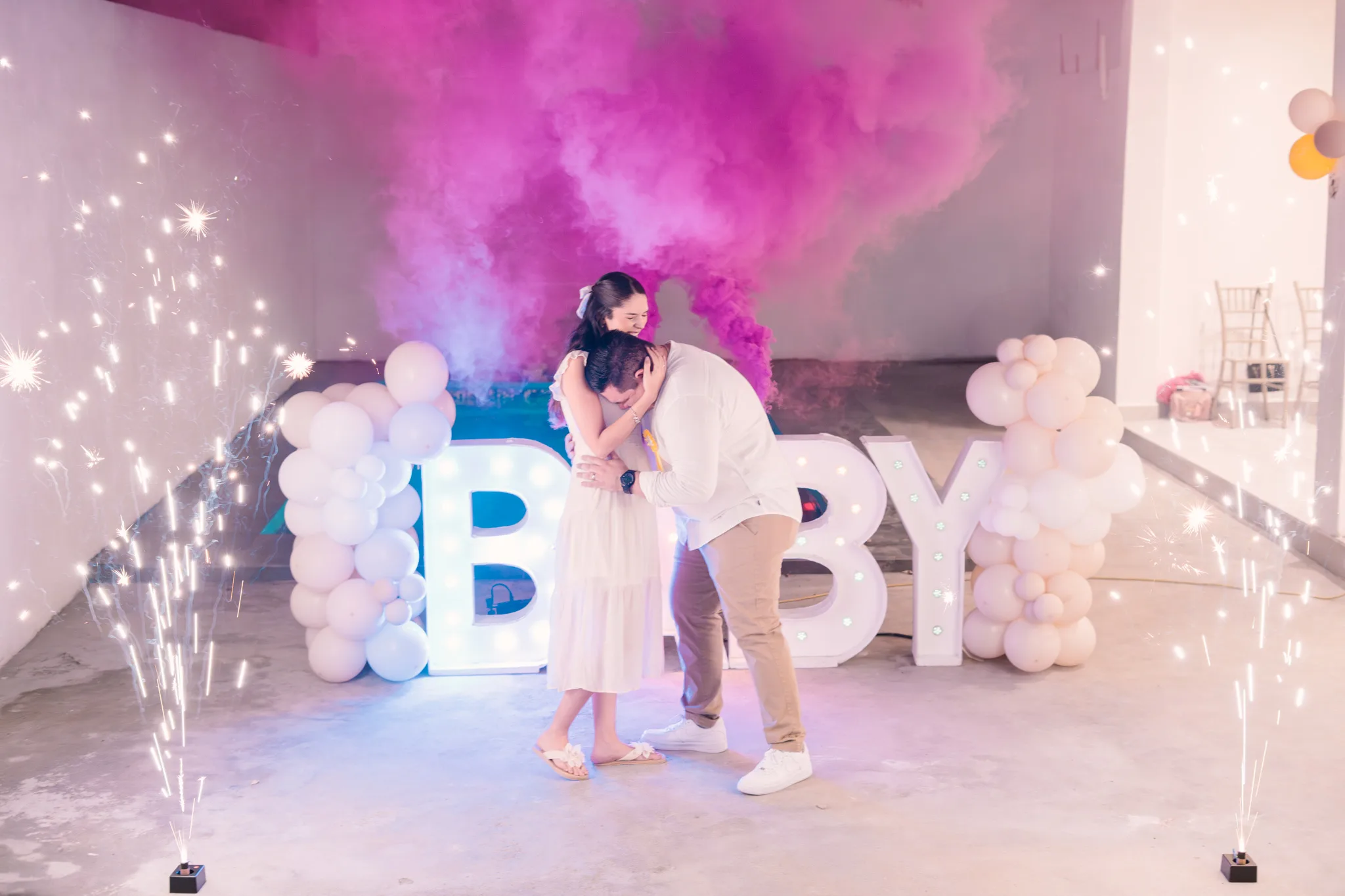 Futuros padres abrazándose emocionados con humo rosa y chispas en fiesta de revelación de género
