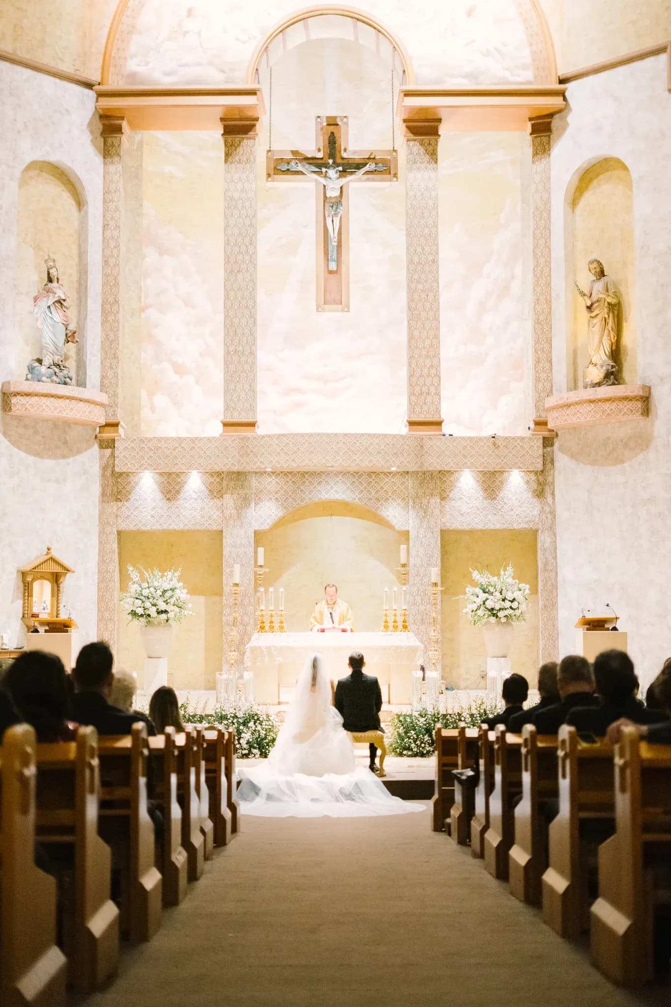 Vista del altar de iglesia católica durante ceremonia de boda con novios arrodillados y sacerdote