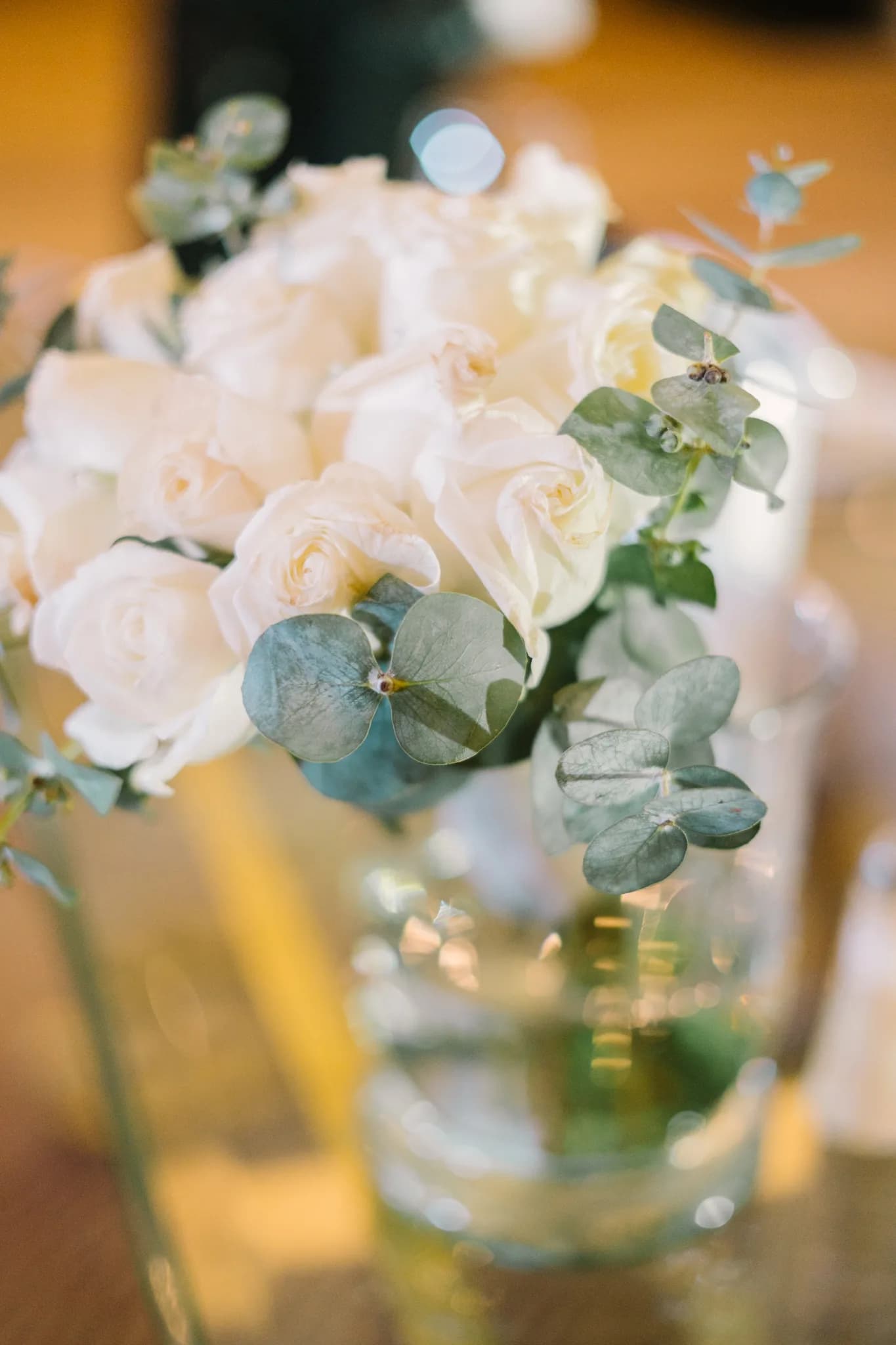 Centro de mesa con rosas blancas y eucalipto en florero de vidrio para decoración de boda