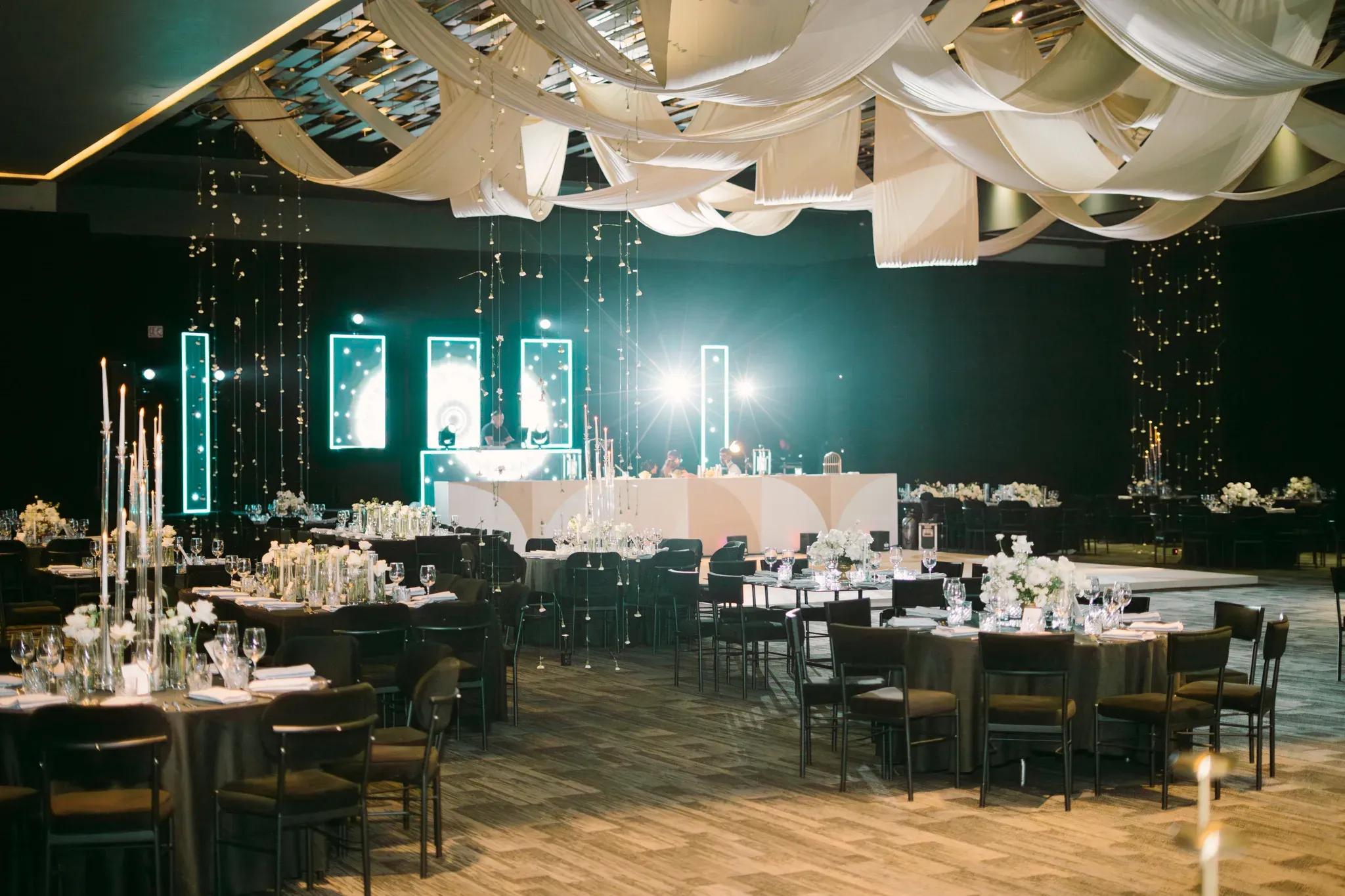 Salón de bodas elegante con decoración de telas blancas en techo, mesas redondas y escenario con luces neón