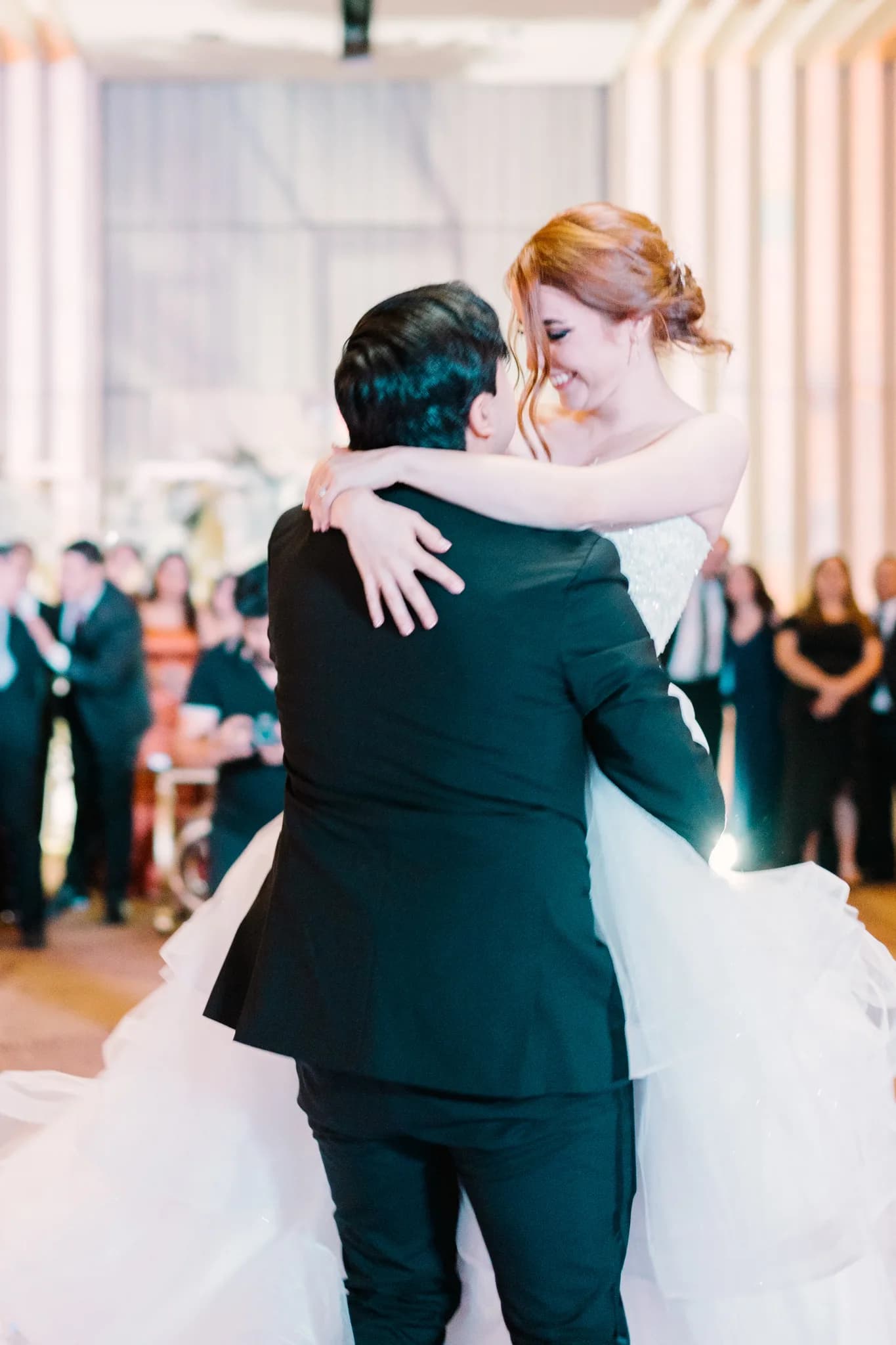 Novia de pelo rojo abrazando al novio sonriendo durante primer baile en recepción de boda