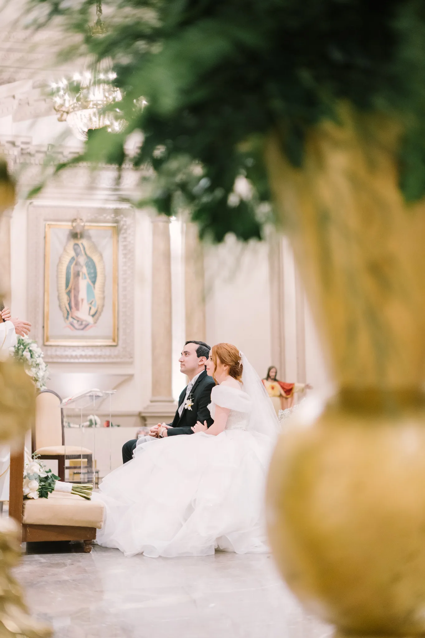 Pareja de novios sentados frente al altar con imagen de la Virgen de Guadalupe en iglesia católica