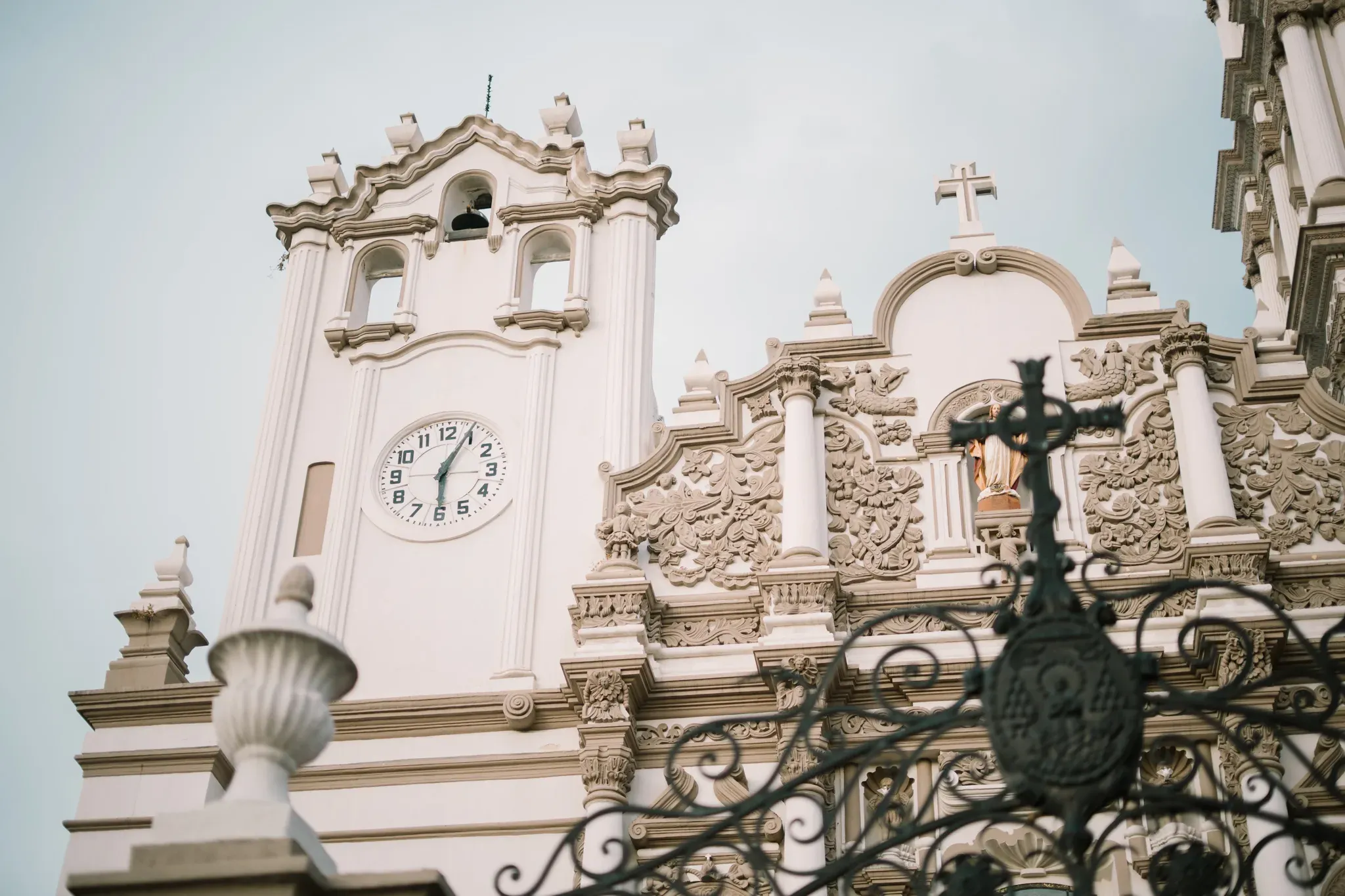 Torre de iglesia barroca blanca con reloj y ornamentos religiosos en Monterrey contra cielo azul
