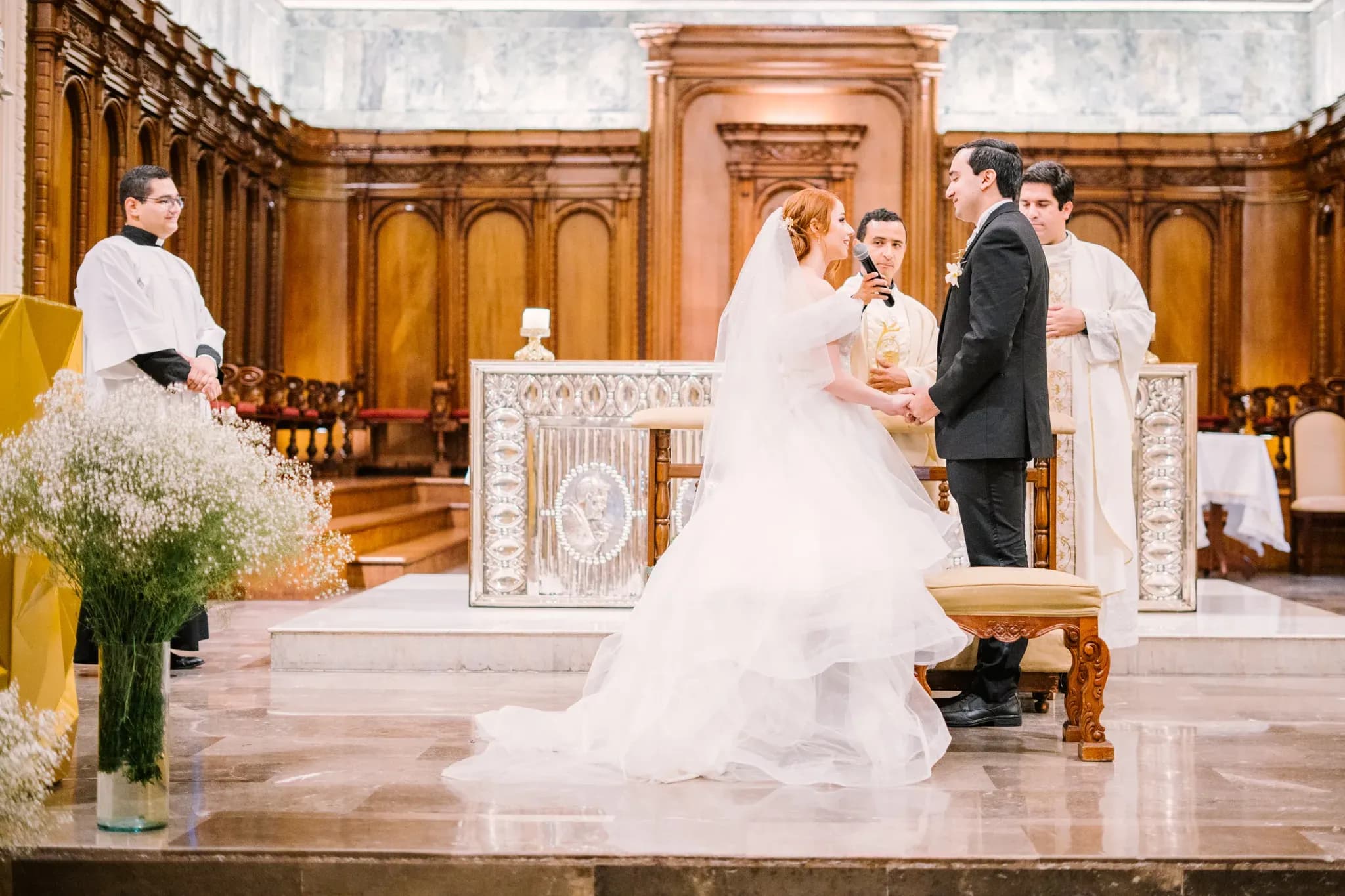 Pareja de novios dando votos matrimoniales tomados de las manos frente al altar de iglesia colonial