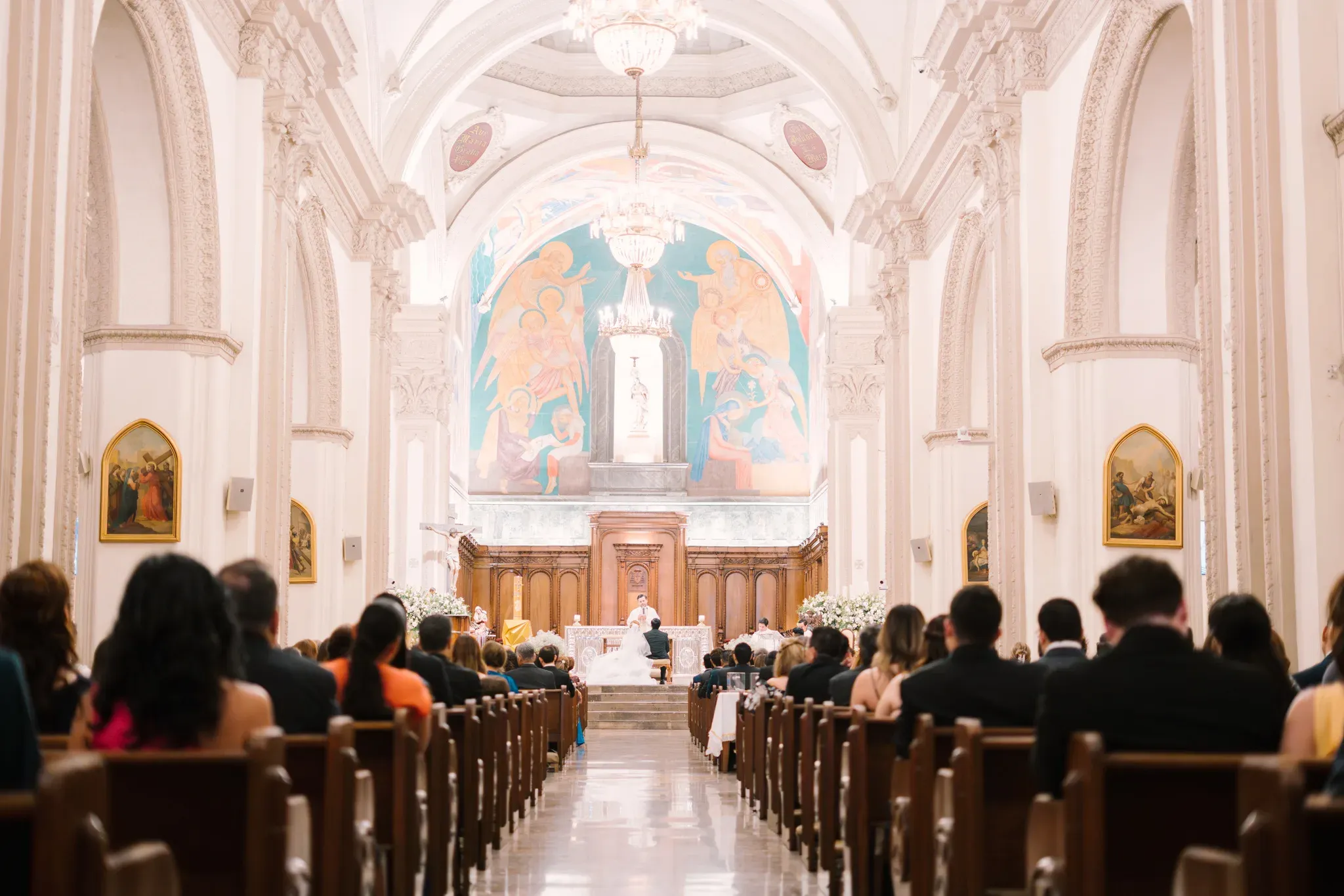 Vista general de iglesia católica llena de invitados durante ceremonia de boda con frescos en ábside