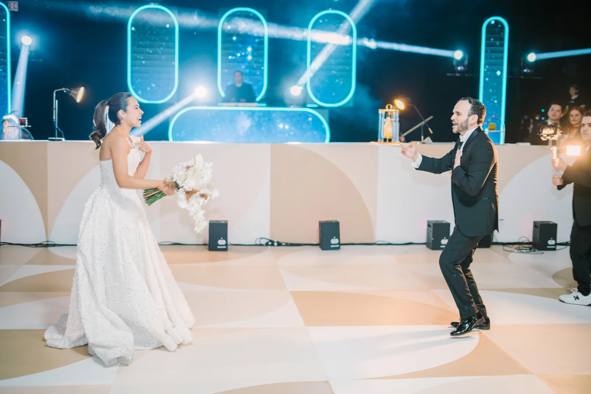 Novios divirtiéndose en pista de baile con luces neón turquesa durante recepción de boda moderna
