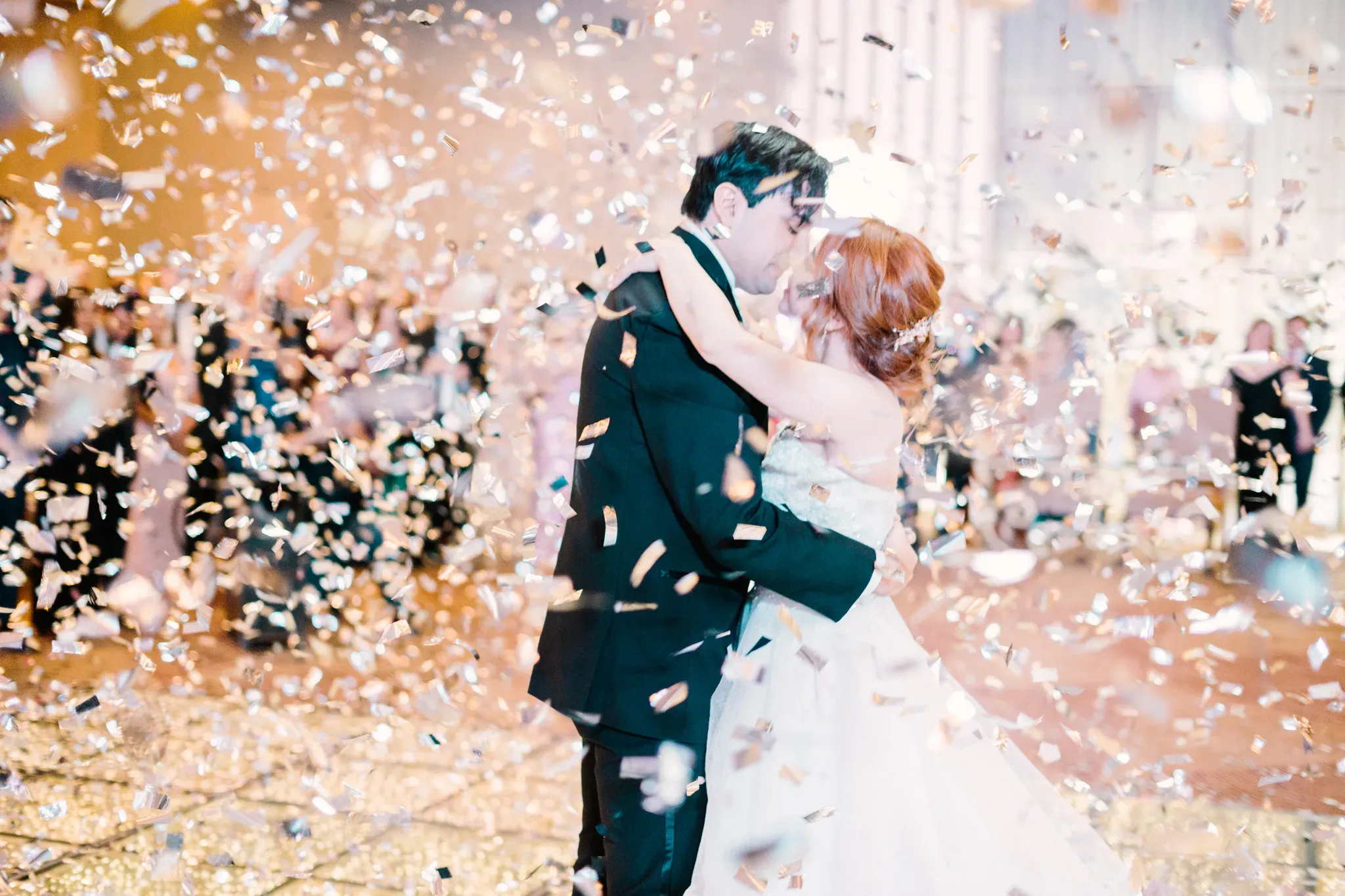Novios besándose en pista de baile rodeados de confeti dorado durante boda elegante